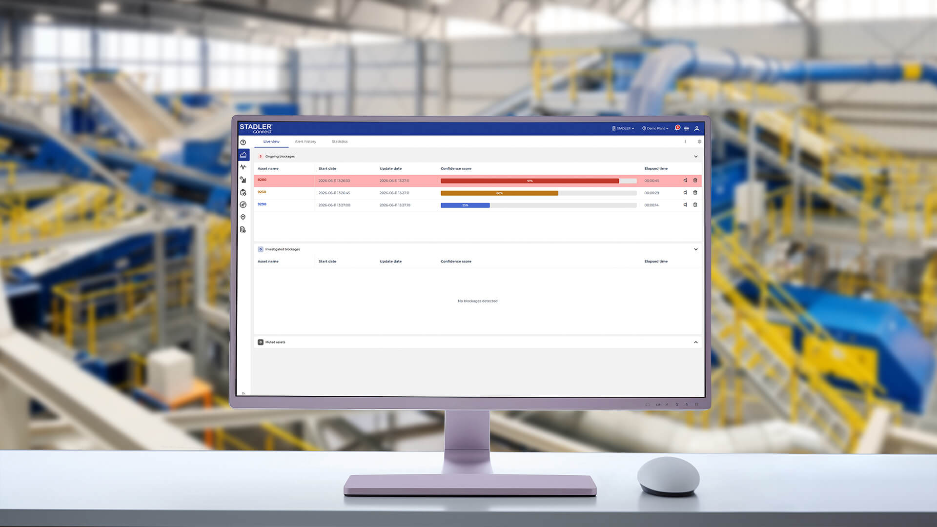 Monitor de sobremesa con el panel de control STADLERconnect Blockage Detection Dashboard para la detección y supervisión de atascos de material en plantas de clasificación de residuos. La interfaz de usuario muestra los atascos actuales con indicaciones de tiempo, mensajes de advertencia codificados por colores y valores de confianza. Al fondo se ve una planta de clasificación de STADLER.